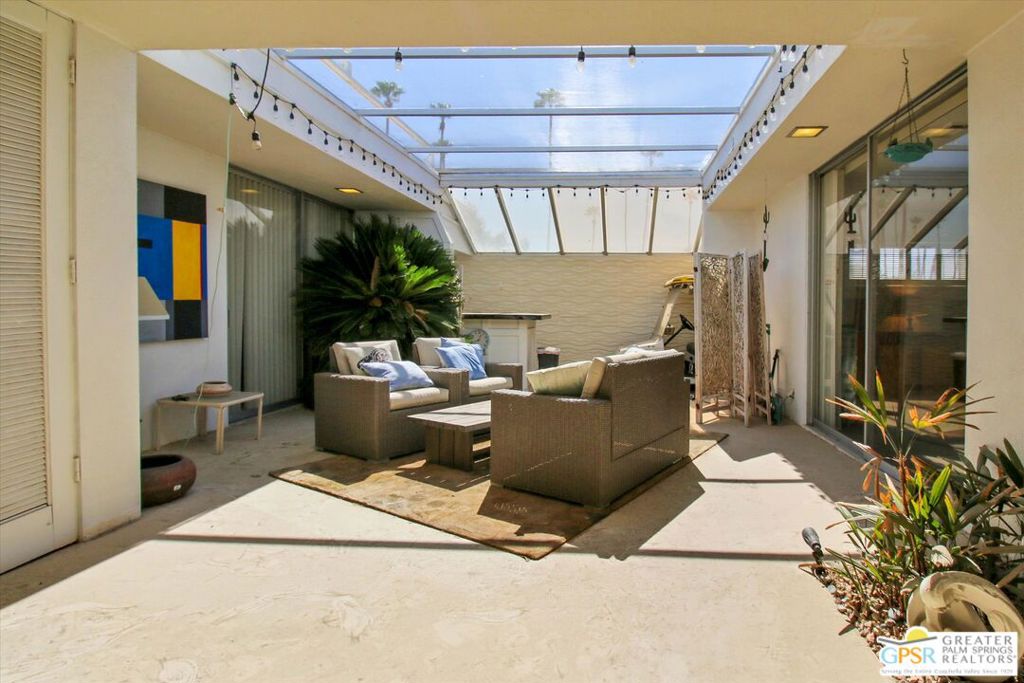 Furnished courtyard patio beneath a glass roof, with wicker seating and tropical plants.