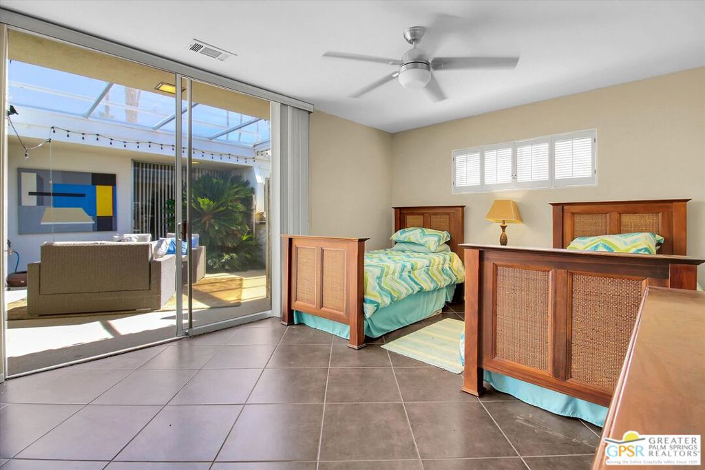 Bedroom with two wooden beds and sliding glass doors opening to a sunny patio.