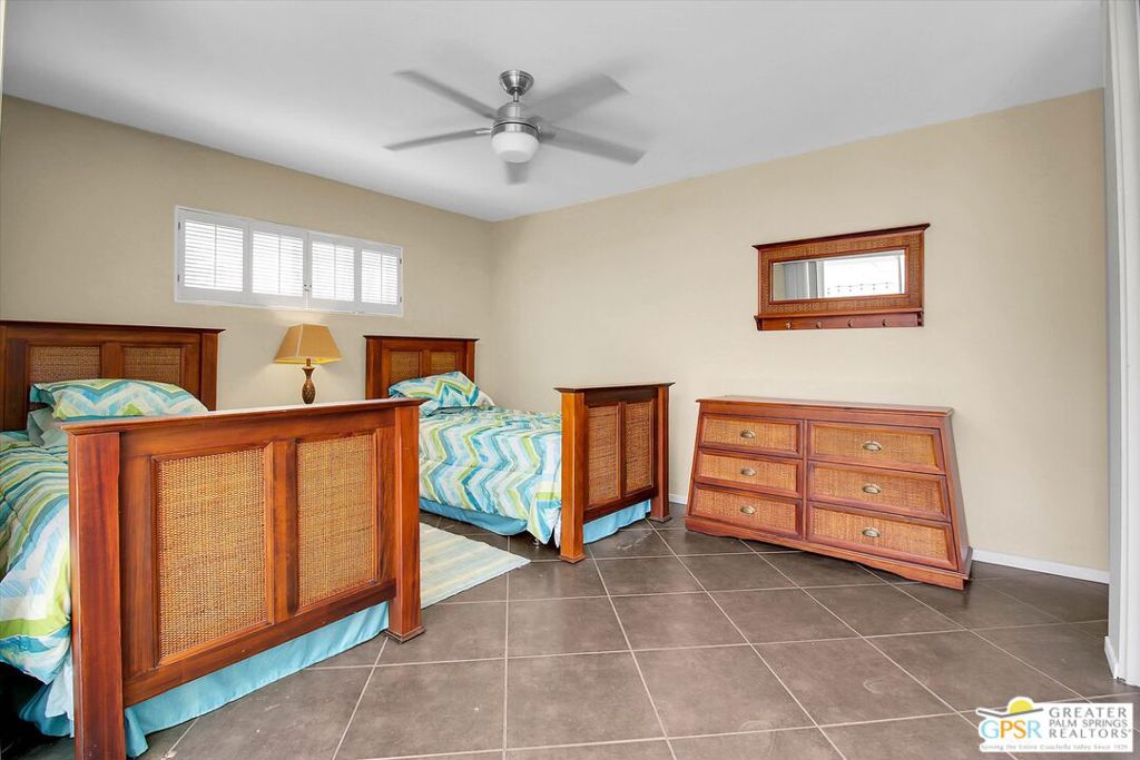 Bedroom with two cane-panel beds, colorful bedding, a matching dresser, and a ceiling fan.