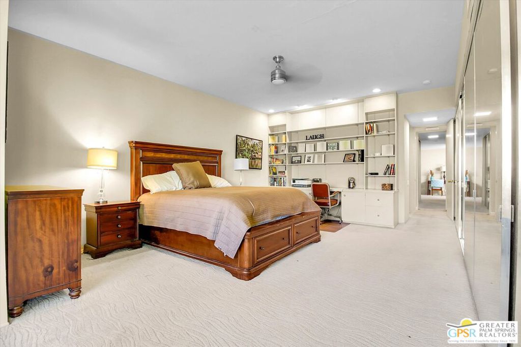 Furnished bedroom with a wooden bed, built-in bookshelves and desk, and mirrored closet doors.