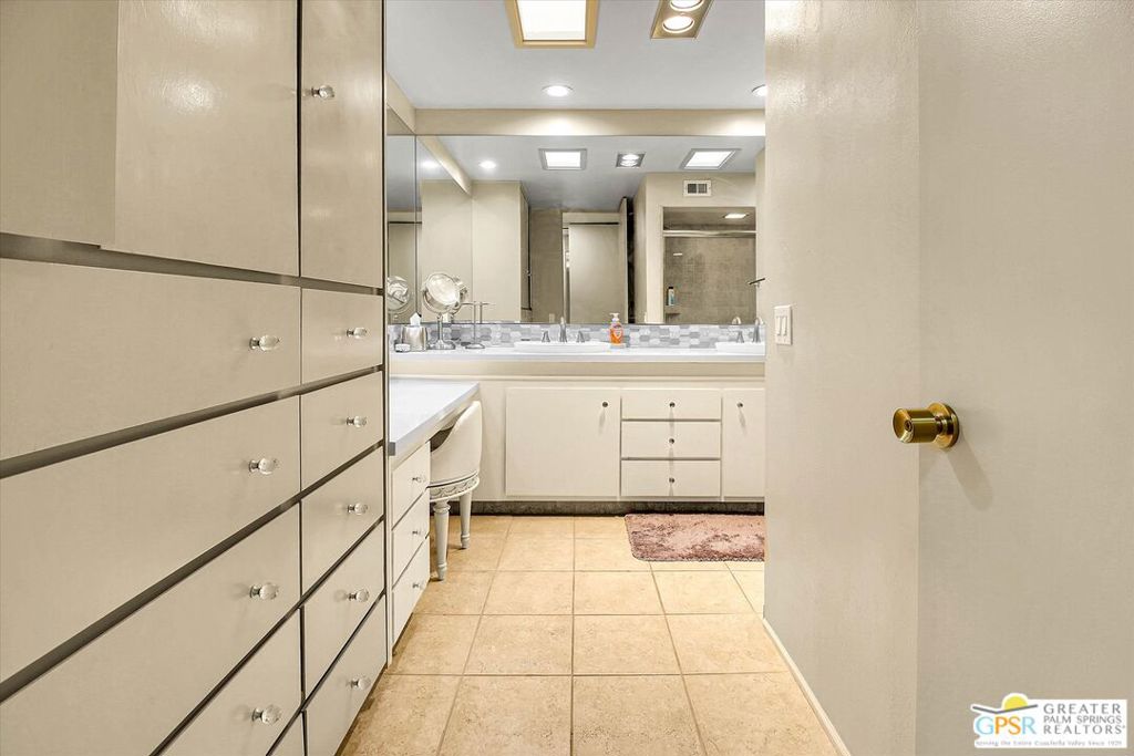 Bathroom with extensive built-in cabinetry, a long mirrored vanity, and beige tile flooring.