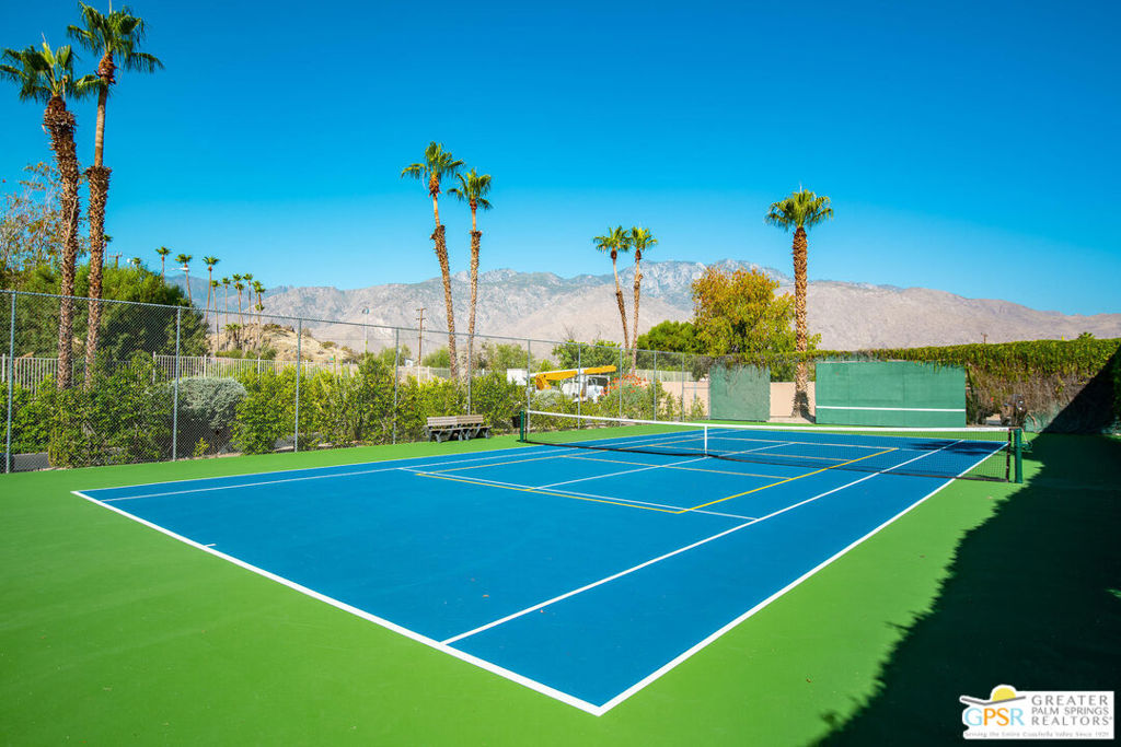 Tennis court with palm trees and mountains in the background.
