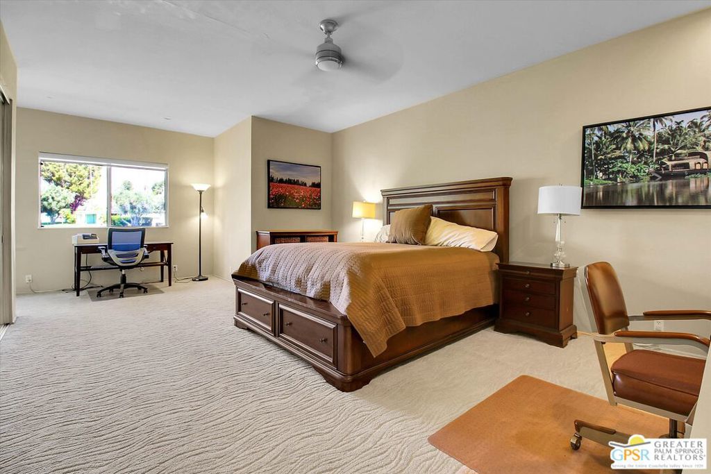 Bedroom with a large wooden bed, desk by the window, and light patterned carpet.