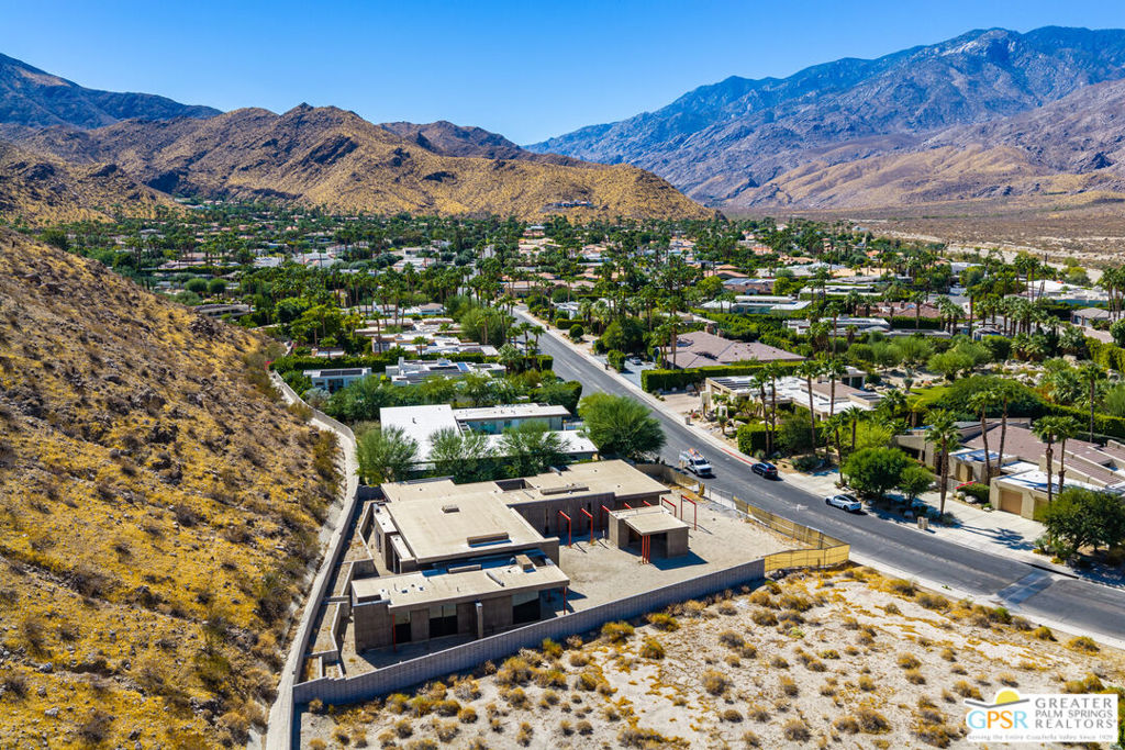 Aerial view of a home under construction beside a road, with Palm Springs neighborhoods and mountains beyond.