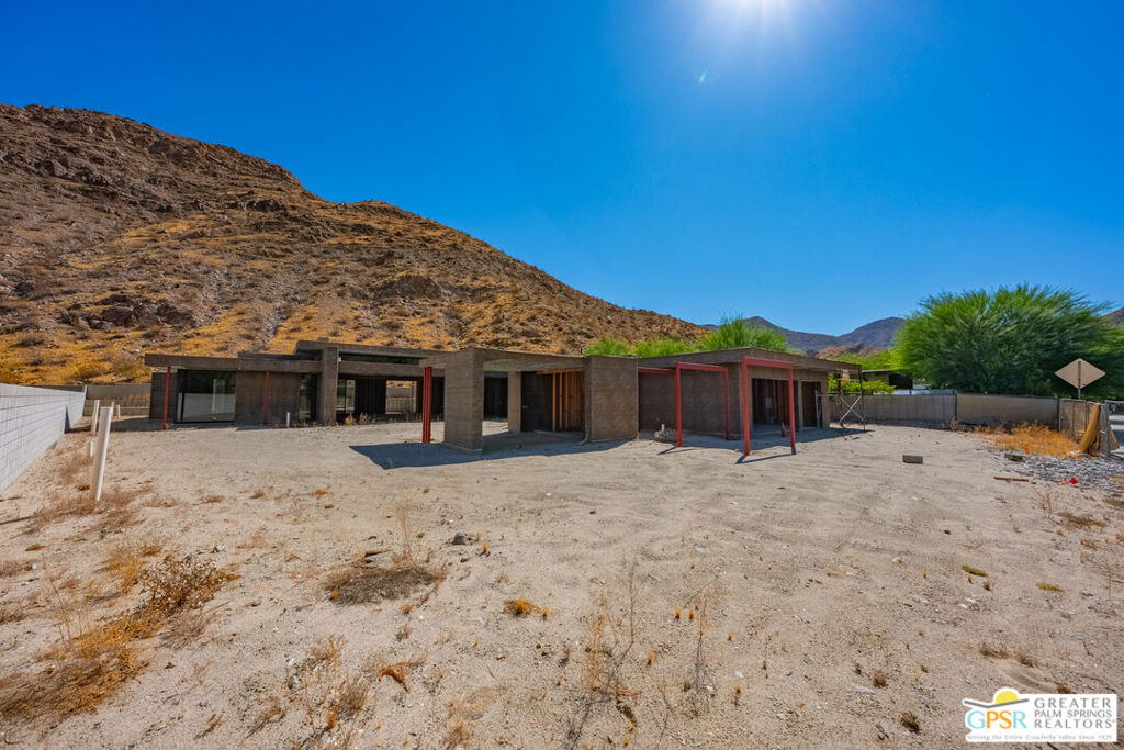 Modern single-story home under construction, with red steel supports and a rocky mountain behind it.