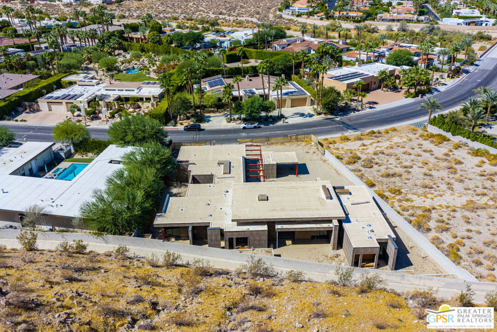 Aerial view of a flat-roofed home under construction, surrounded by desert landscaping and neighboring homes.