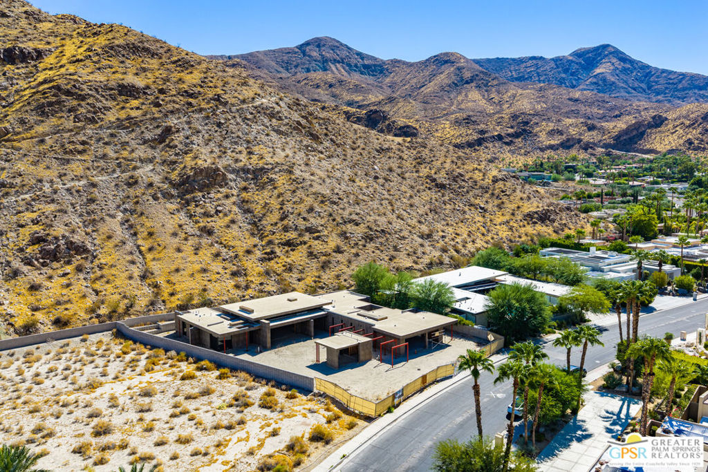 Aerial view of a flat-roof home at the base of desert hills, with mountains beyond.