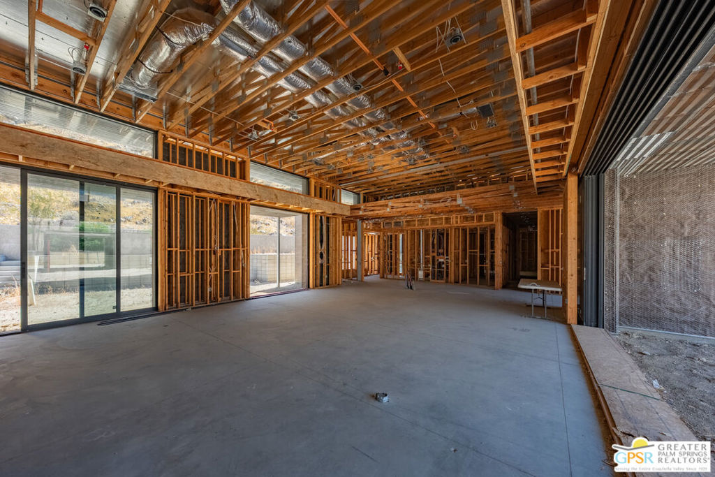 Unfinished interior with exposed timber framing, ceiling ductwork, concrete floor, and sliding glass doors.