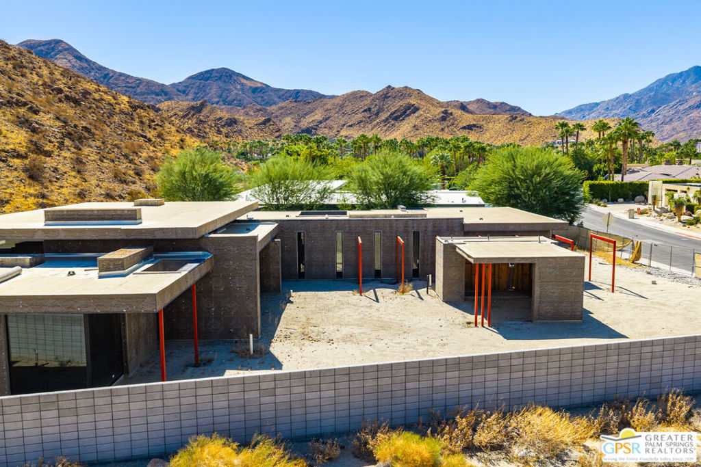 Modern home under construction on a walled lot, with desert mountains in the background.