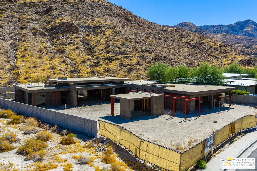Modern flat-roofed home under construction below a rocky desert hillside.