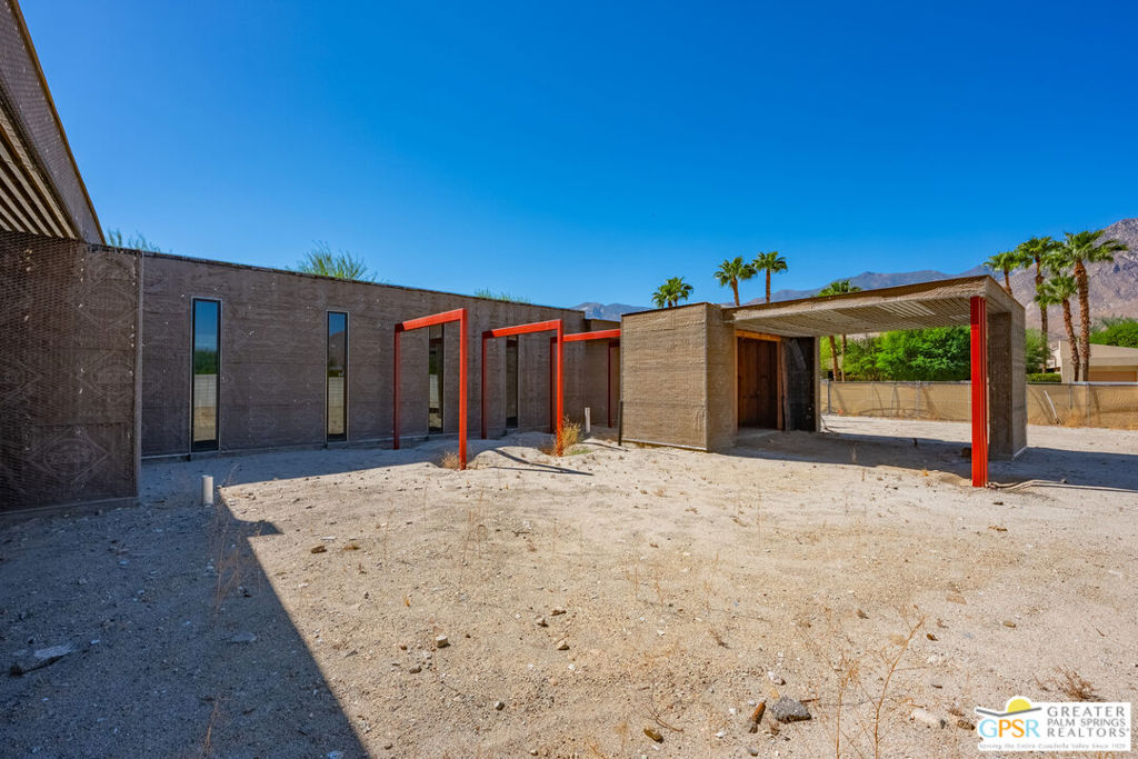 Modern home under construction with red steel framing and a gravel courtyard.