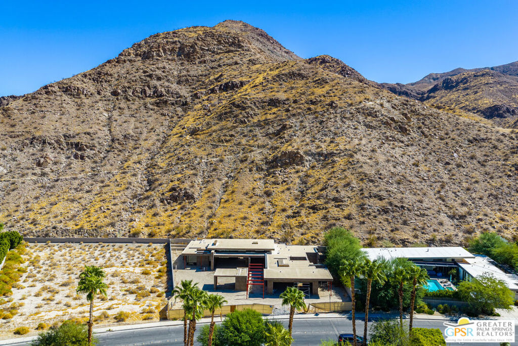 Aerial view of a modern home with a pool beneath a rocky desert mountain.