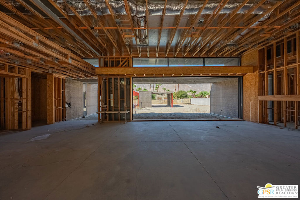 Unfinished home interior with exposed framing, ceiling ductwork, and a wide opening to the yard.