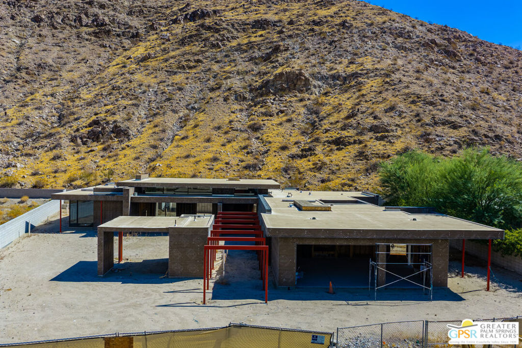 Modern flat-roof home under construction at the base of a rocky desert hillside.