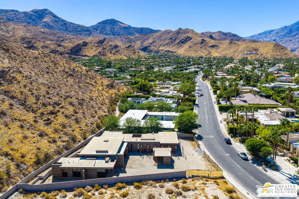 Aerial view of a modern home under construction beside a street, with Palm Springs mountains beyond.