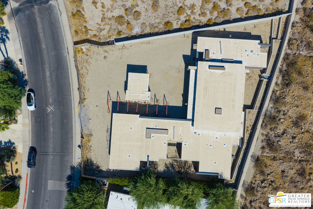 Aerial view of a flat-roofed home beside a road, surrounded by desert terrain and palm trees.