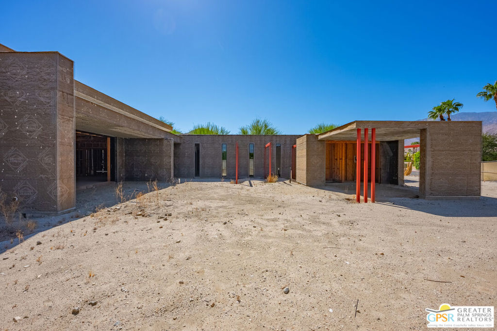 Unfinished modern concrete home with red supports and a sandy yard in Palm Springs.