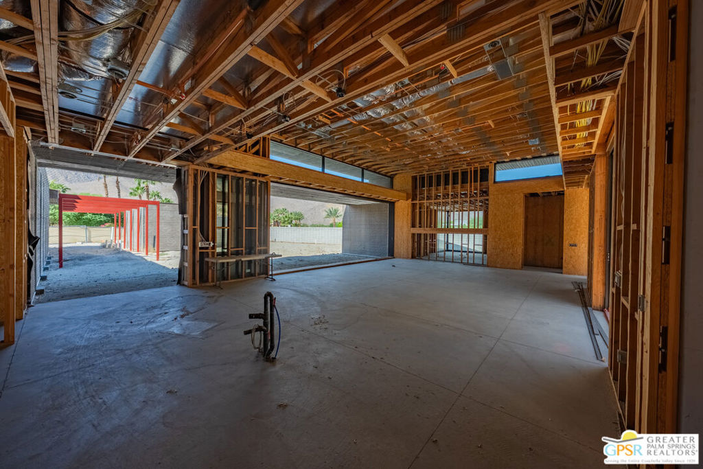 Unfinished garage with exposed wooden framing, concrete floor, and a wide open exterior doorway.