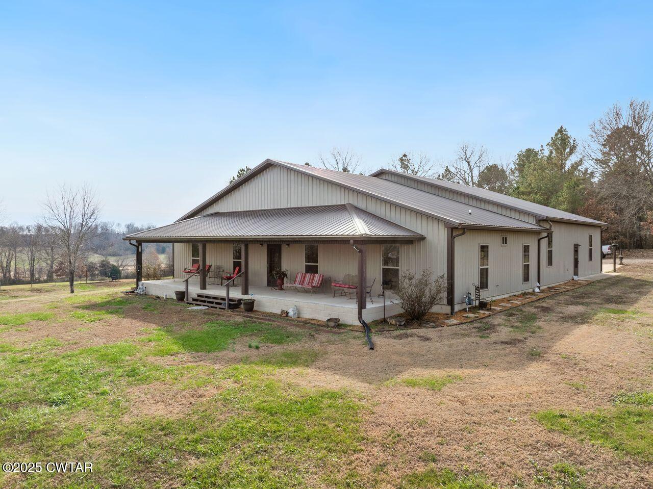 Metal-sided home with a covered, furnished porch and broad lawn.