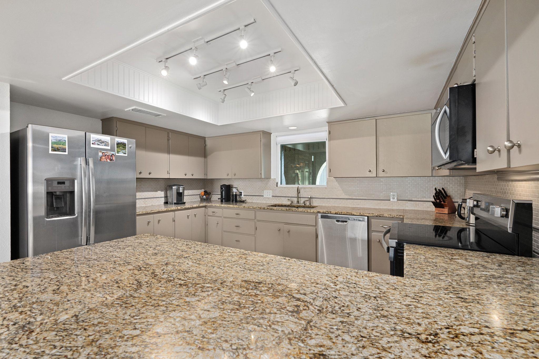 Kitchen with an expansive granite island, taupe cabinetry, stainless steel appliances, and ceiling track lighting.