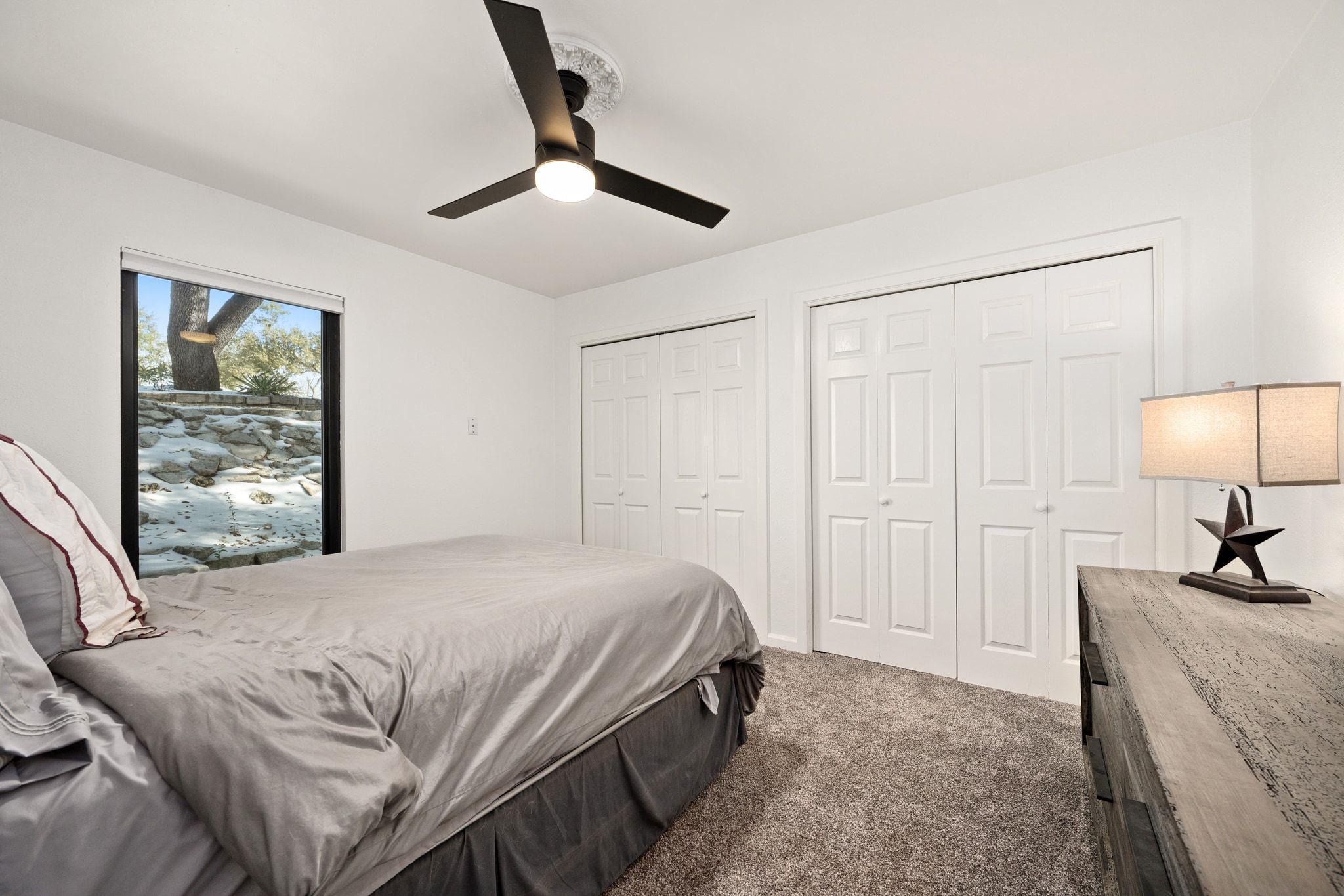 Bedroom with a gray bed, white closet doors, and a window overlooking a rocky garden.
