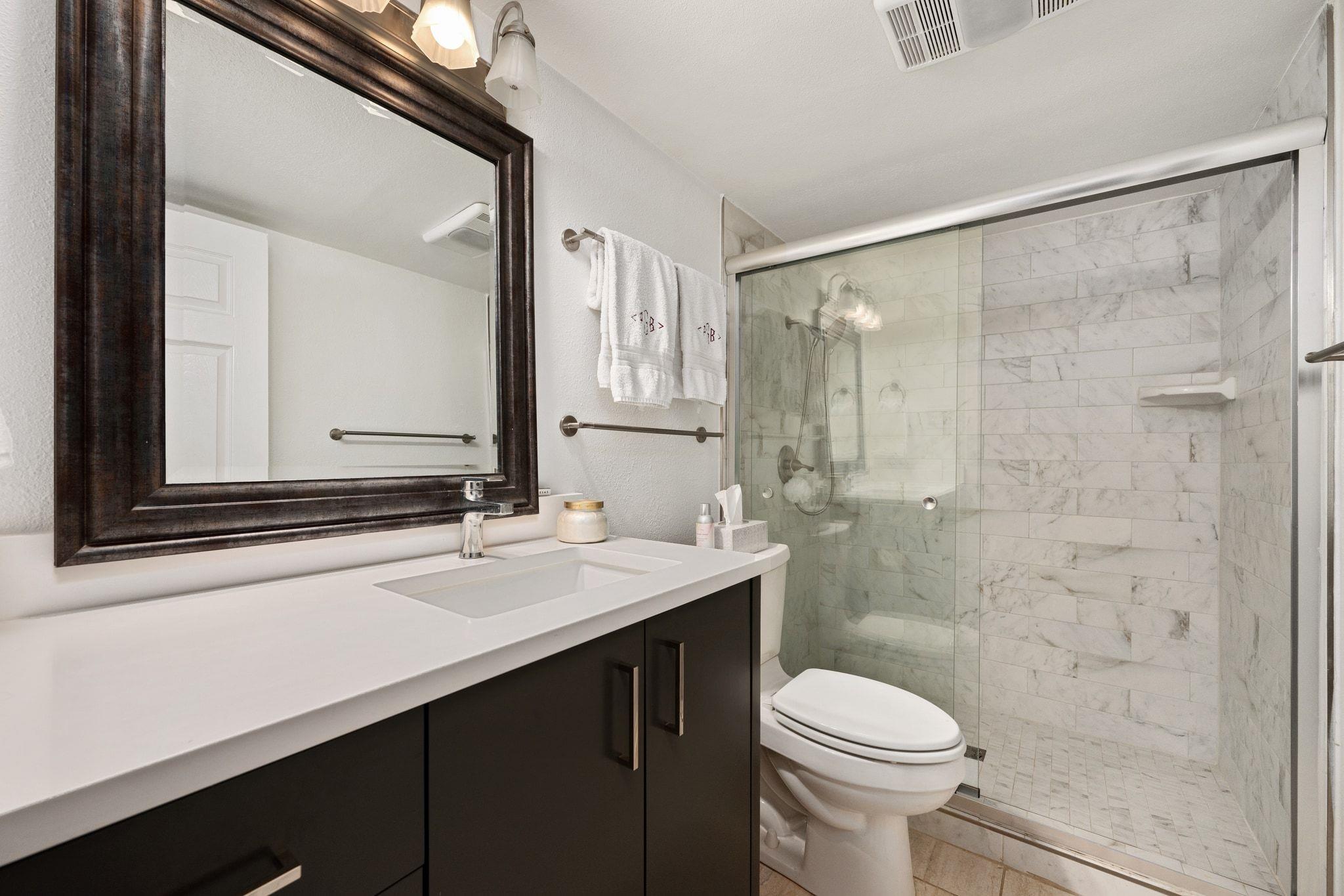 Bathroom with a dark vanity and glass-enclosed marble-tile shower.