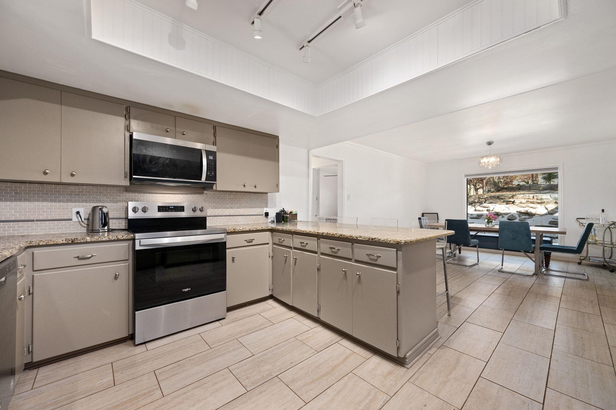 Kitchen with taupe cabinets, granite peninsula, stainless appliances, and an adjoining dining area.