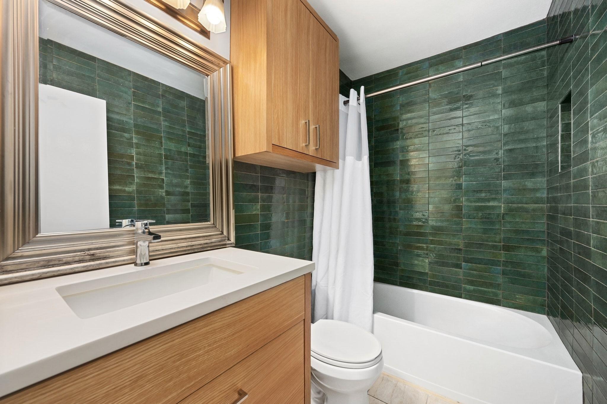 Bathroom with dark green tile, a white bathtub, and a wood vanity beneath a large mirror.