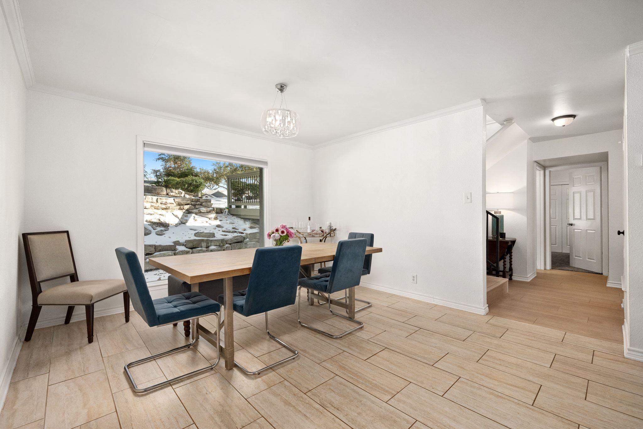 Dining room with a wood table and blue chairs beside a window overlooking a snow-dusted terrace.