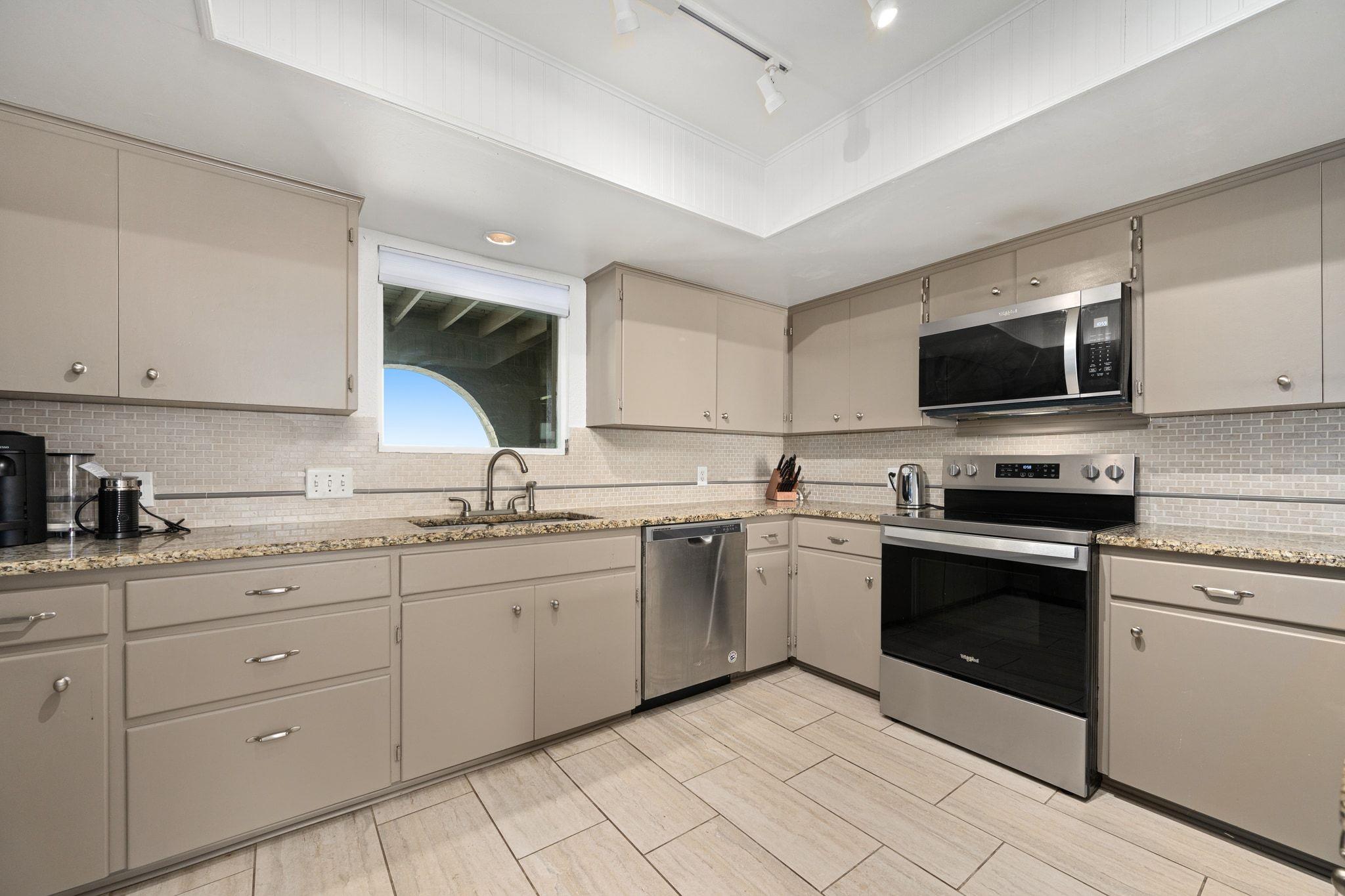 Kitchen with taupe cabinets, granite counters, stainless steel appliances, and a window above the sink.