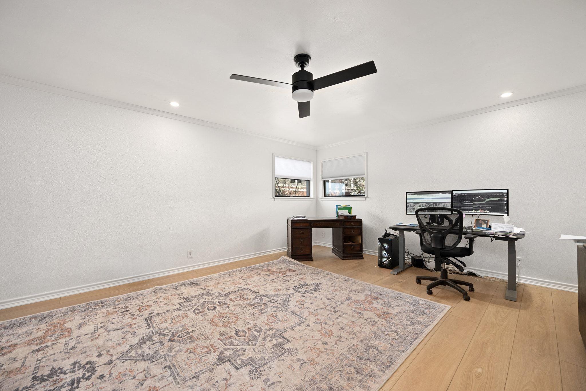 Bright home office with dual monitors, two desks, and a patterned rug.