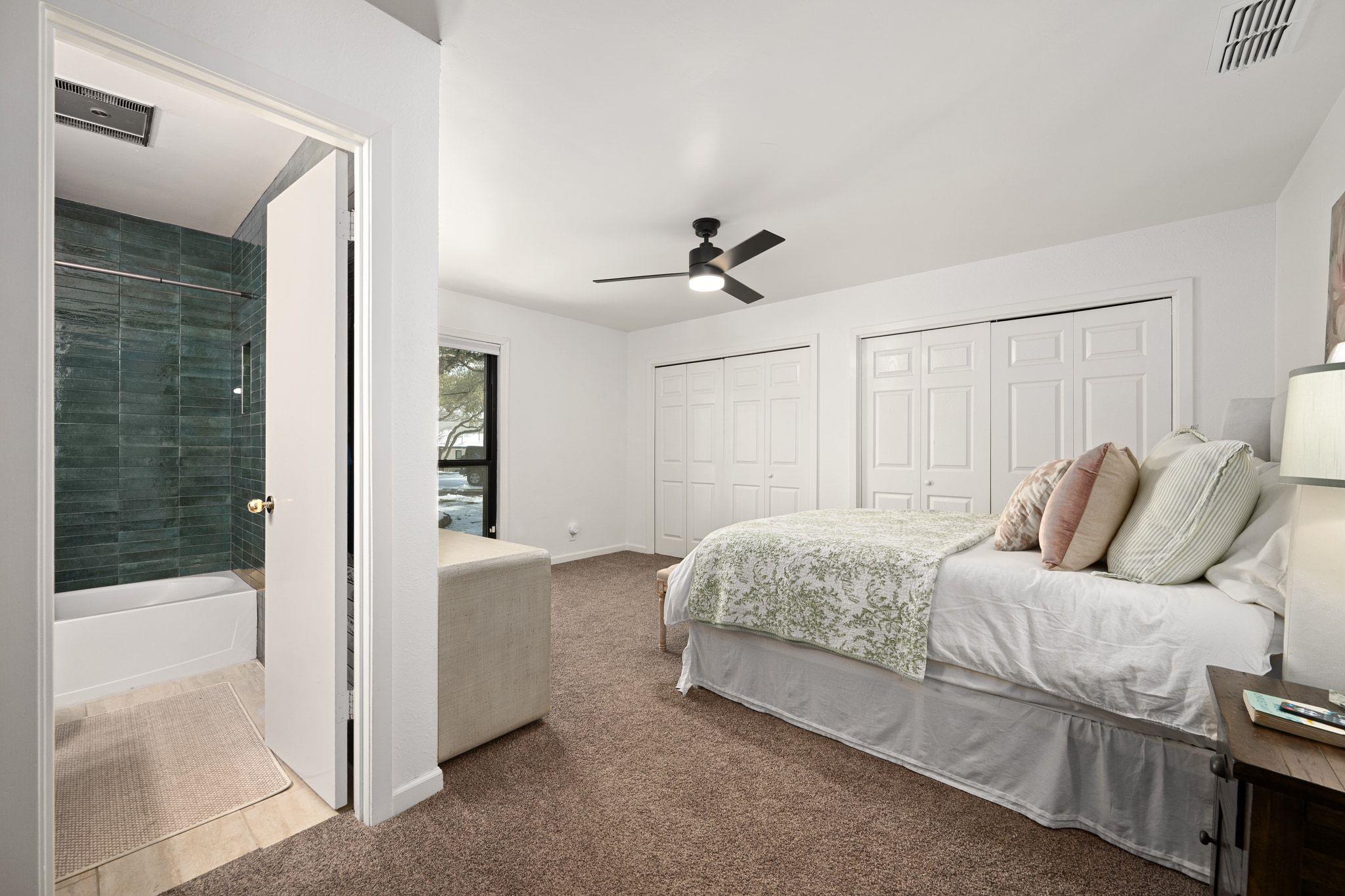 Bedroom with a large bed and brown carpet, opening to a bathroom with dark green tiled walls.