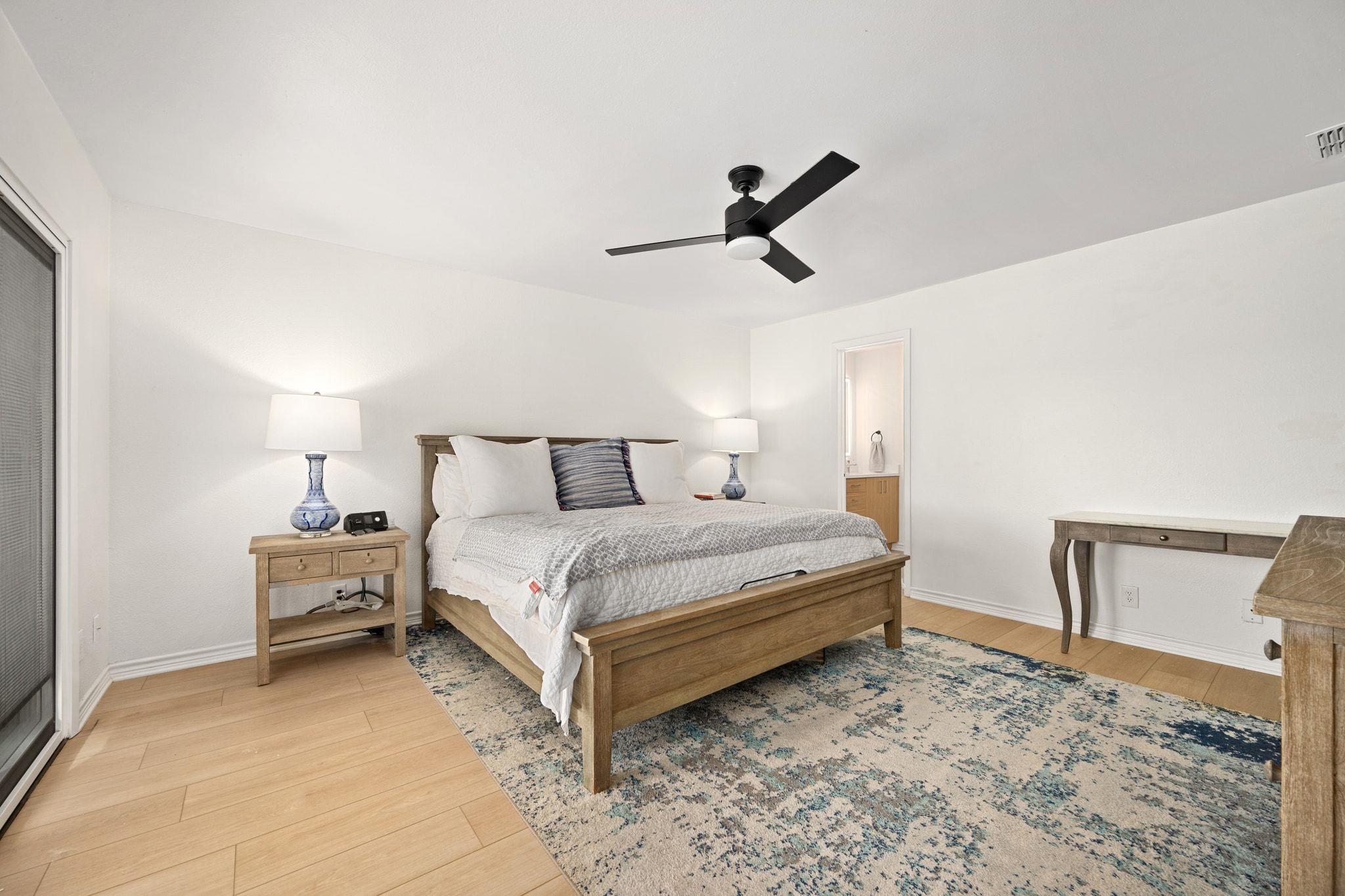 Furnished bedroom with a wooden bed, black ceiling fan, and blue patterned rug.