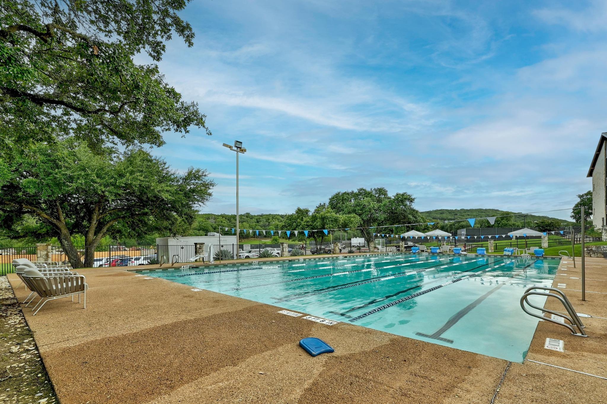 Outdoor lap pool with lane ropes, lounge chairs and mature shade trees.