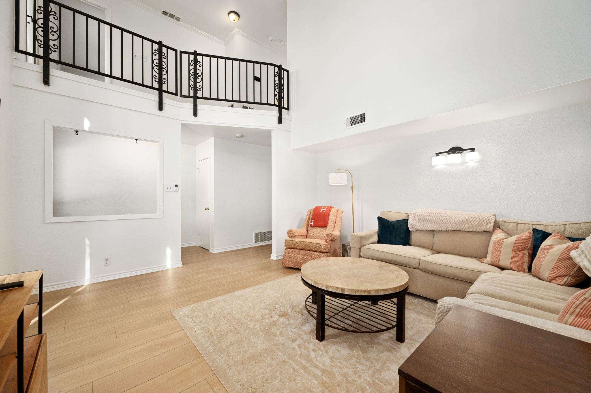 Living room with a beige sectional, round coffee table, and black-railed upstairs landing.