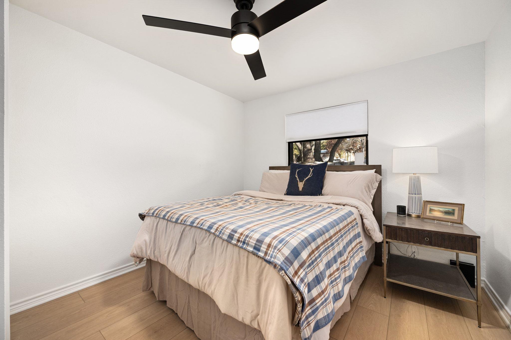 Furnished bedroom with a blue plaid throw, dark ceiling fan, and bedside table.
