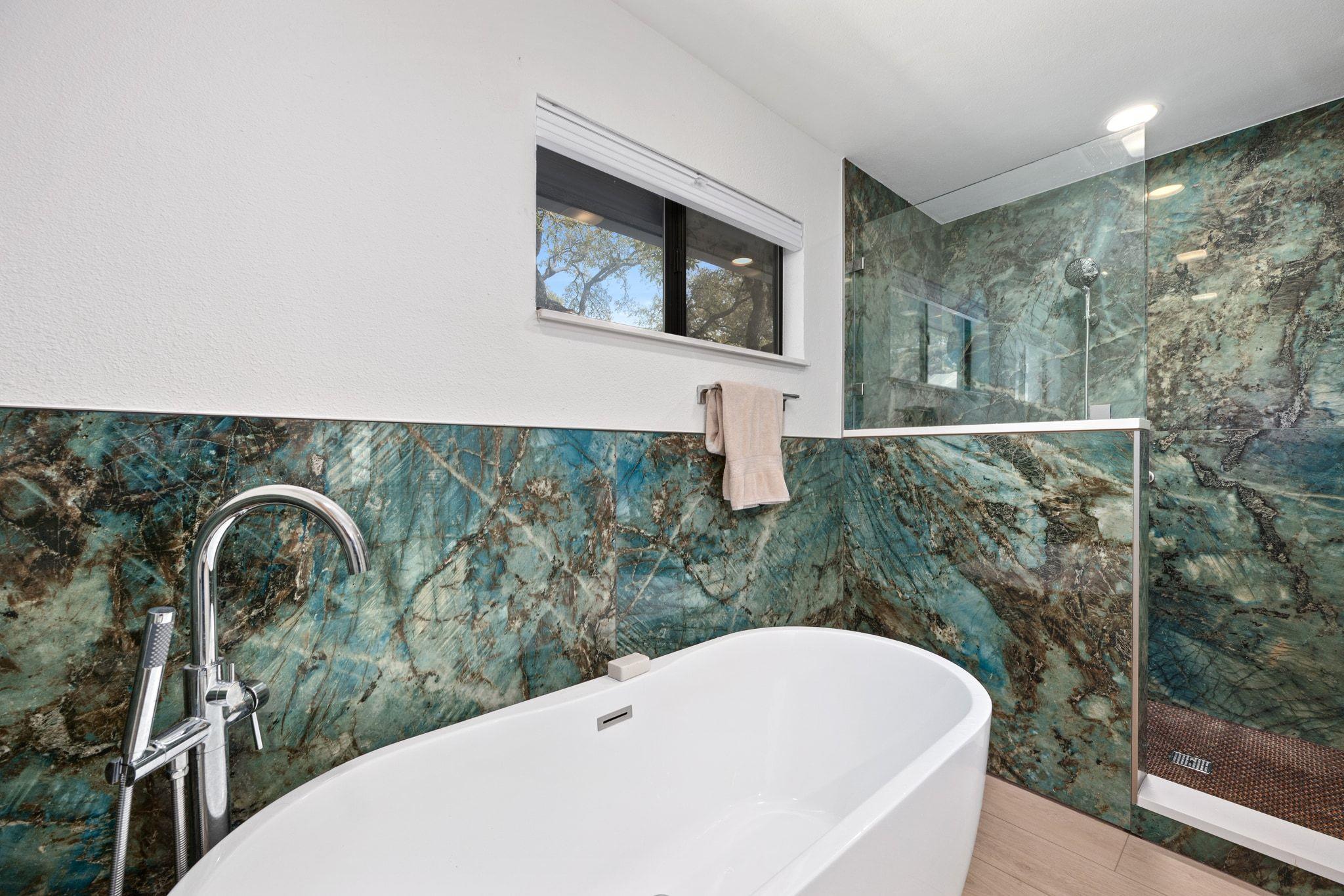 Bathroom with a white freestanding tub, glass shower, and striking blue-green stone walls.