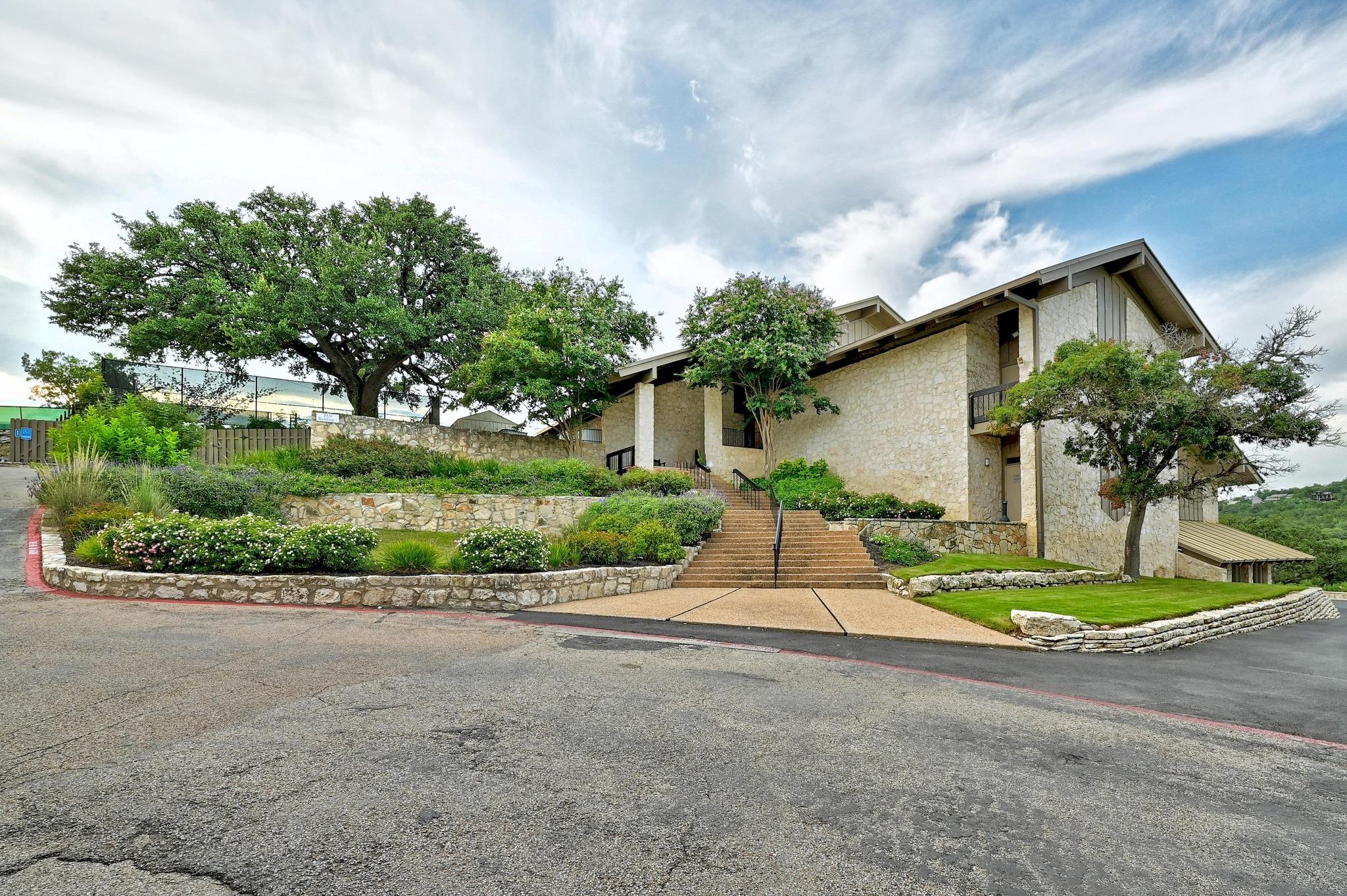 Stone-clad property with landscaped terraces, mature trees, and wide entrance steps.