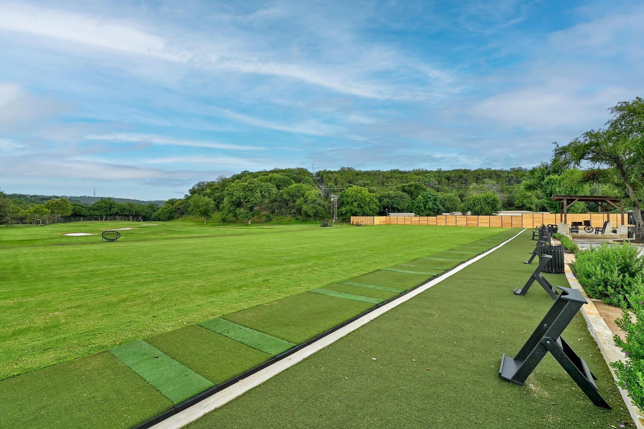 Golf practice area with putting green, turf lanes, and a covered seating pavilion.
