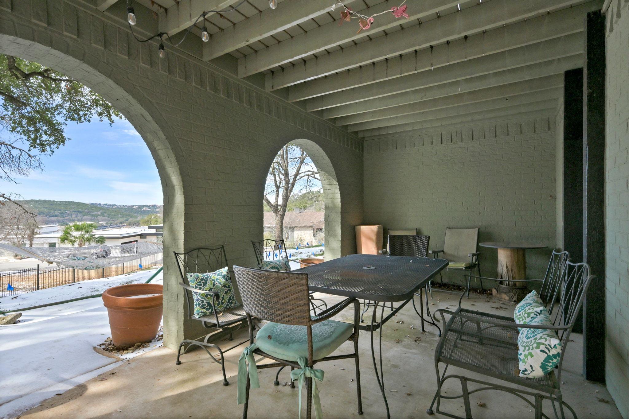 Covered patio with an outdoor dining set, brick arches, and a view of snowy hills.