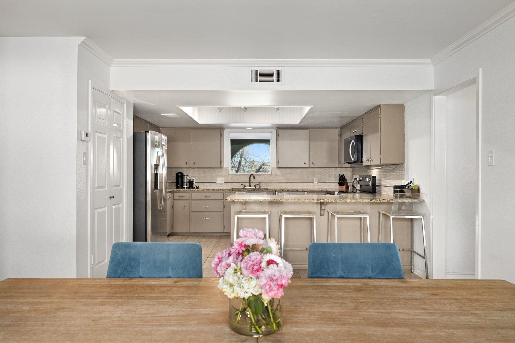 Kitchen with taupe cabinets, stainless appliances, and a granite island behind a flower-topped dining table.