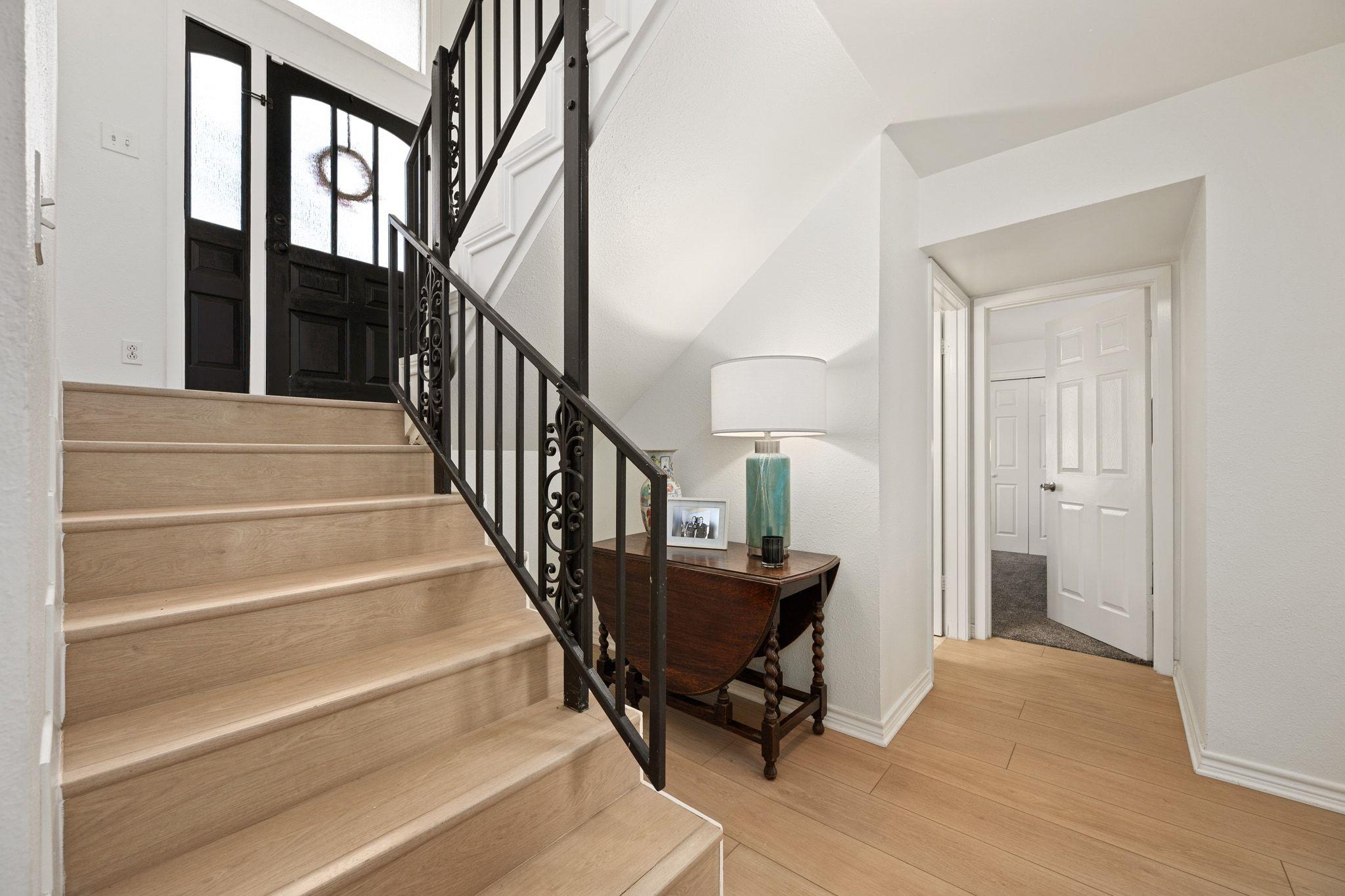 Entryway with light wood stairs, black iron railing, and a console table beneath the stairs.