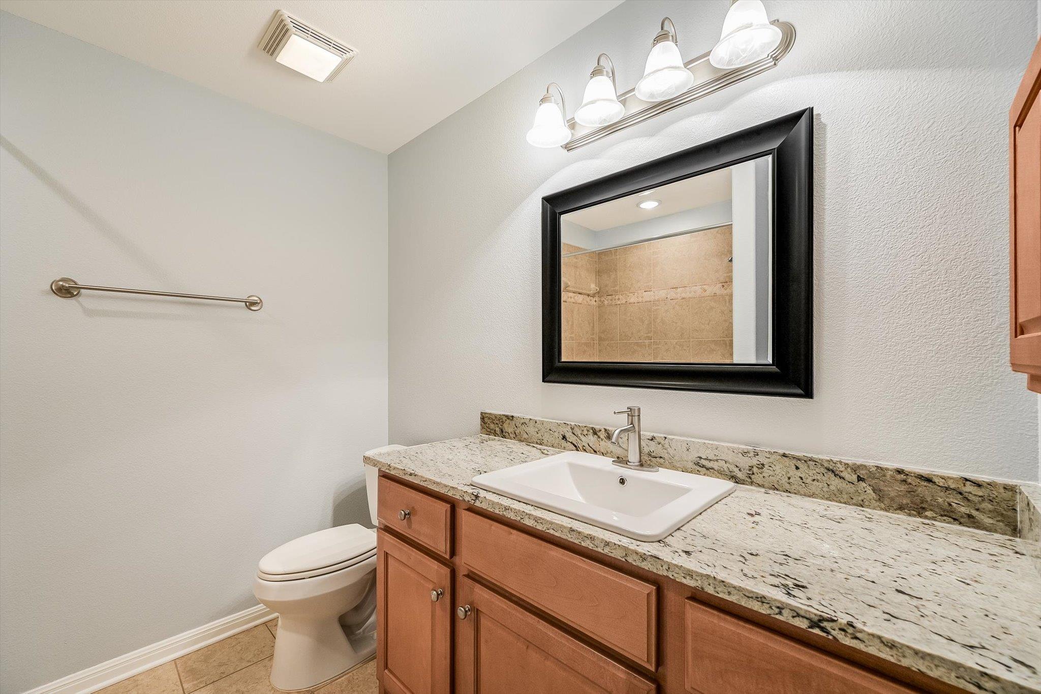 Bathroom with granite vanity, warm wood cabinets, and a large black-framed mirror.