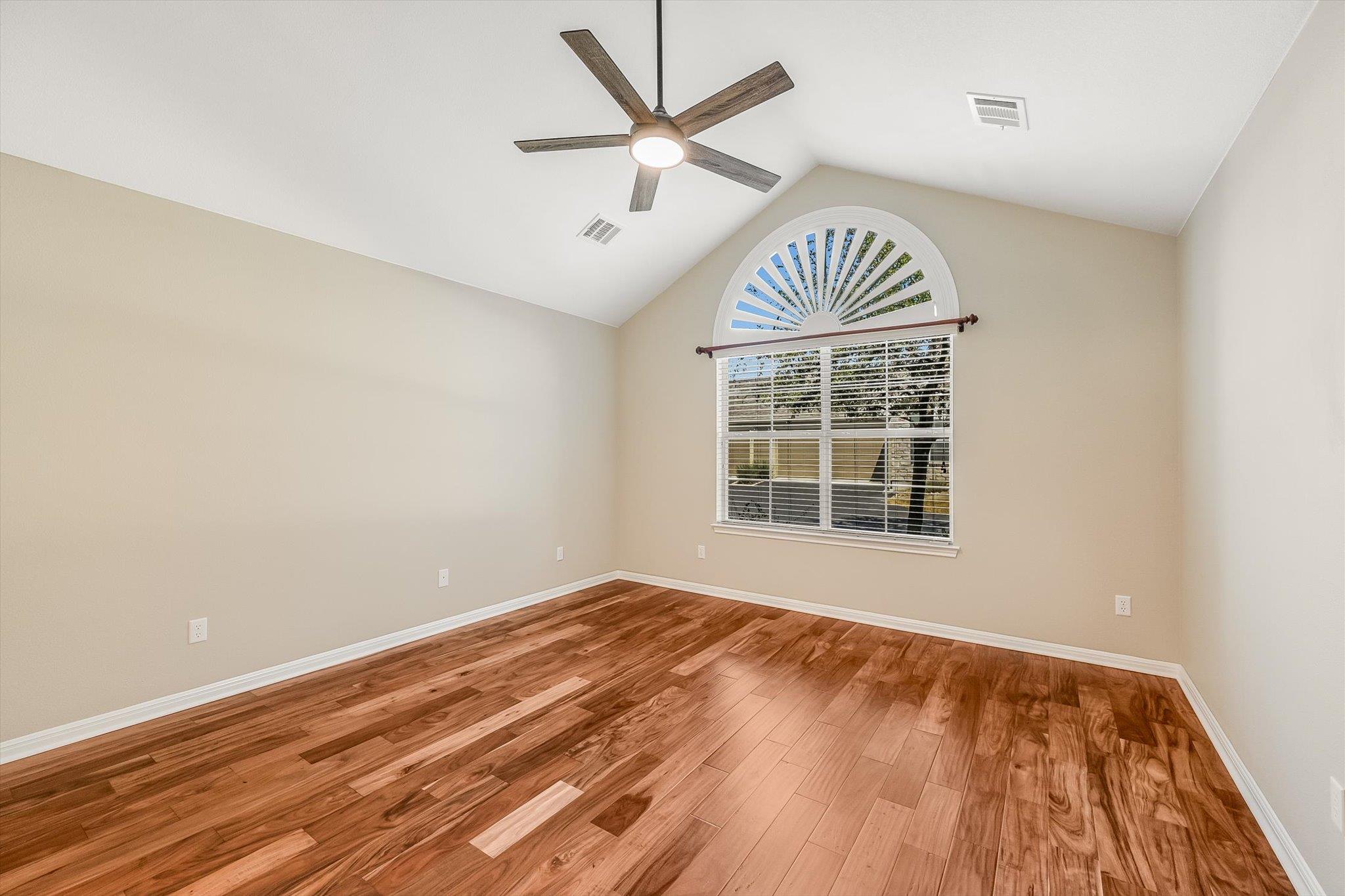 Empty room with hardwood floors, a ceiling fan, and a large arched window.