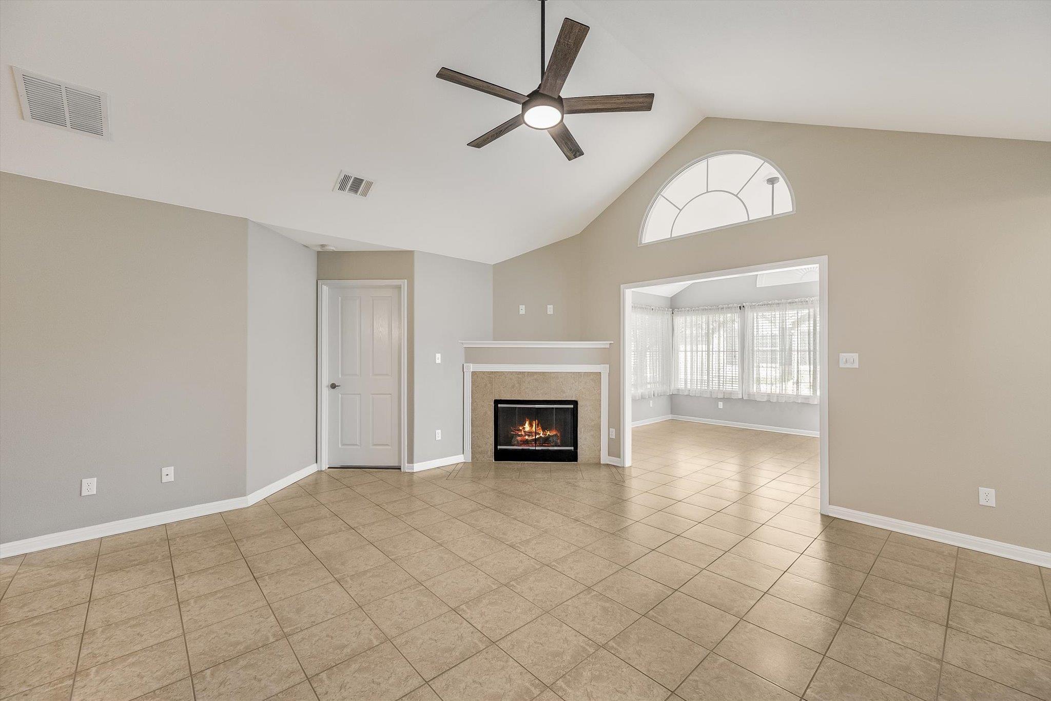 Vacant living room with a tiled floor, fireplace, vaulted ceiling, and arched window.