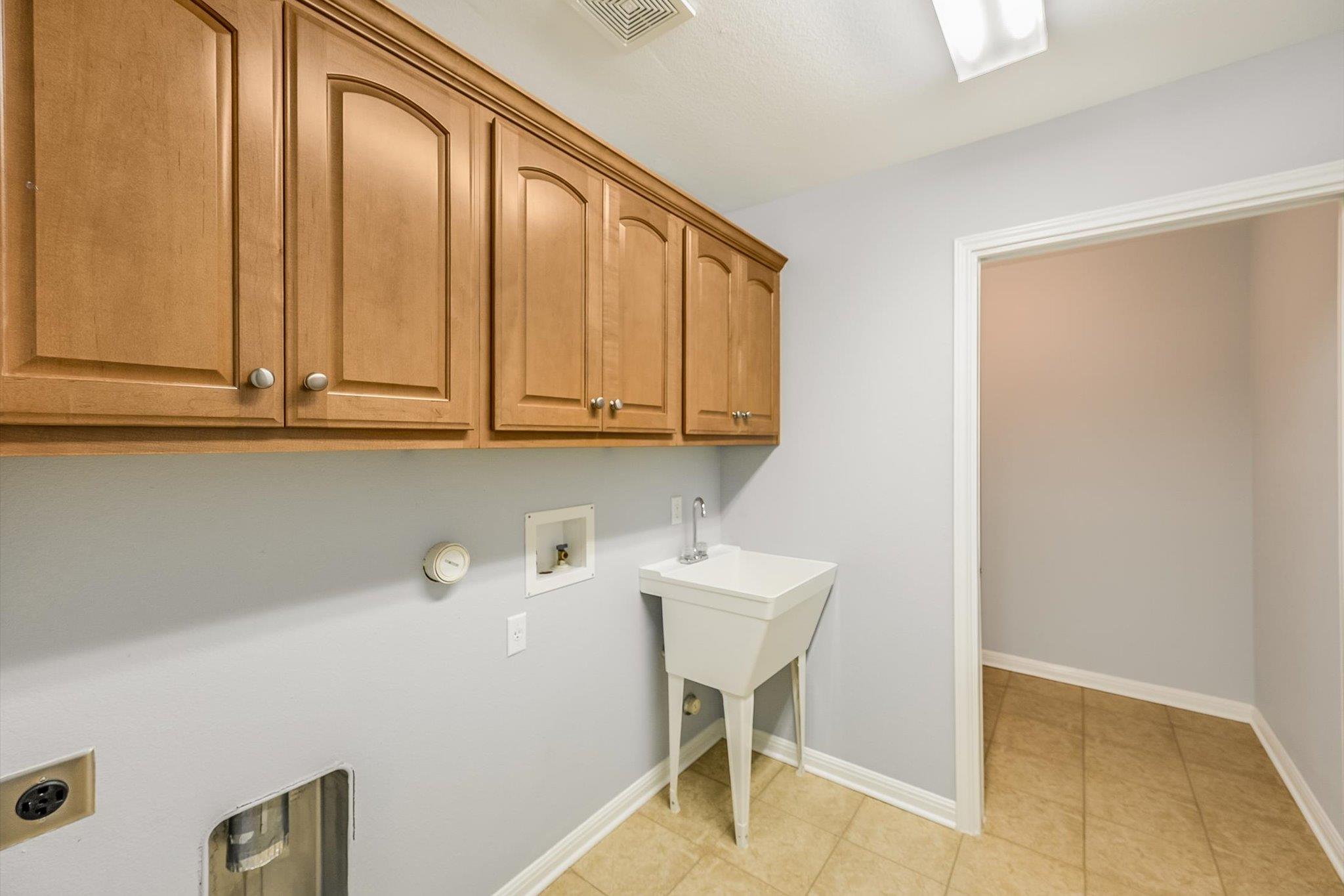 Laundry room with wooden cabinets, washer hookups, and a white utility sink.