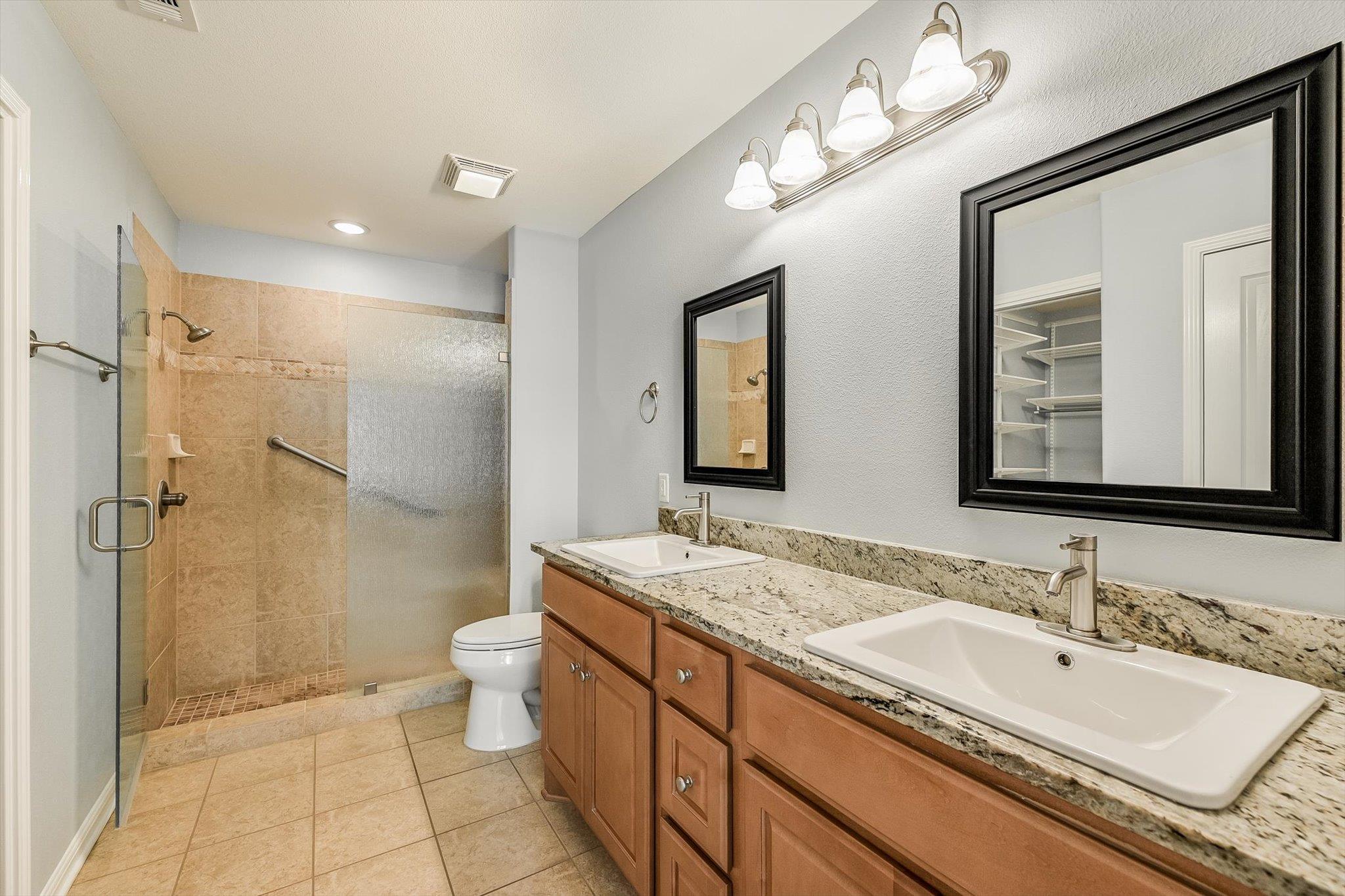 Bathroom with double vanity, granite counter, and tiled walk-in shower with frosted glass.