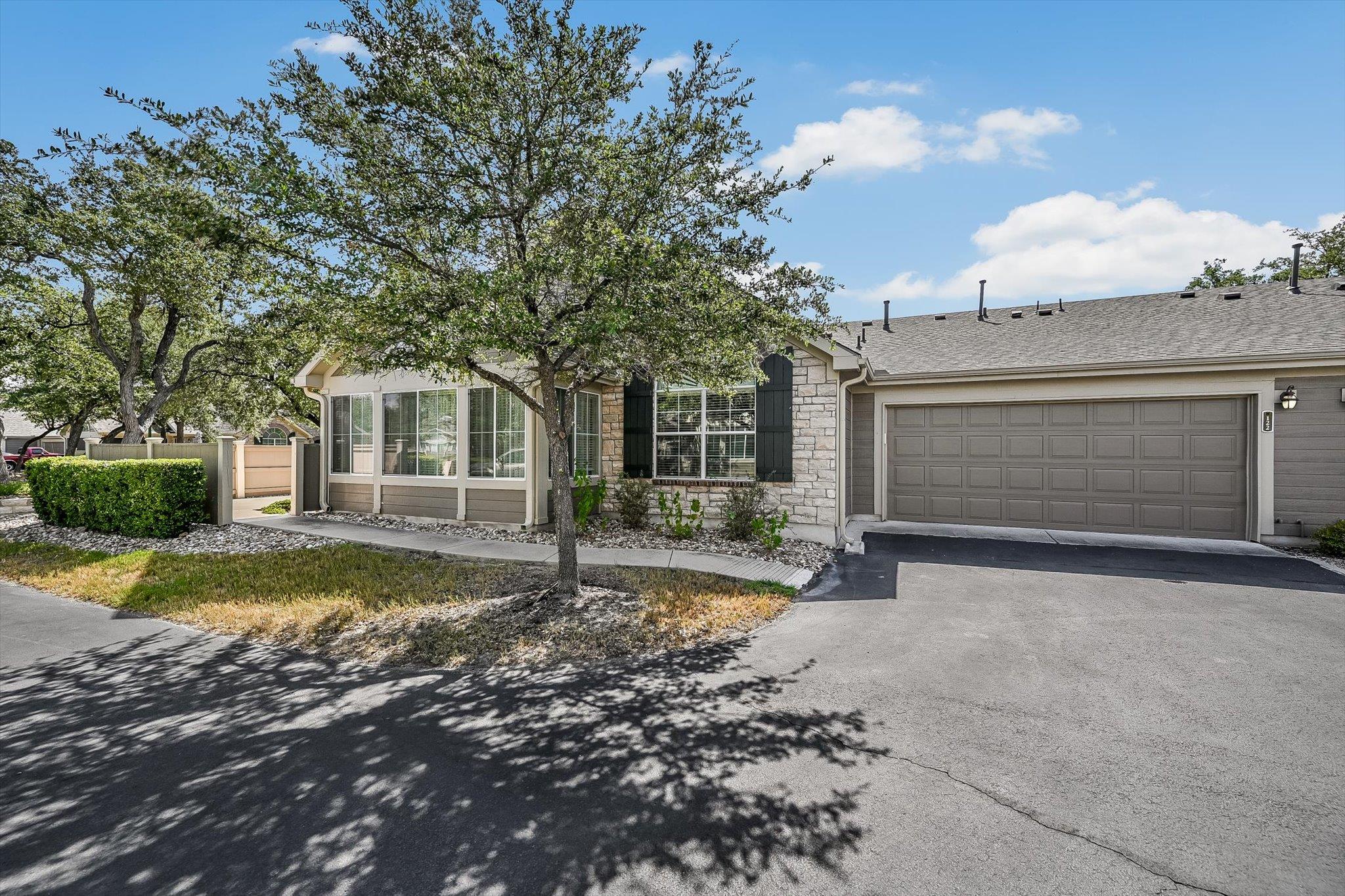 Single-story stone-and-siding home with an attached garage and mature shade trees.