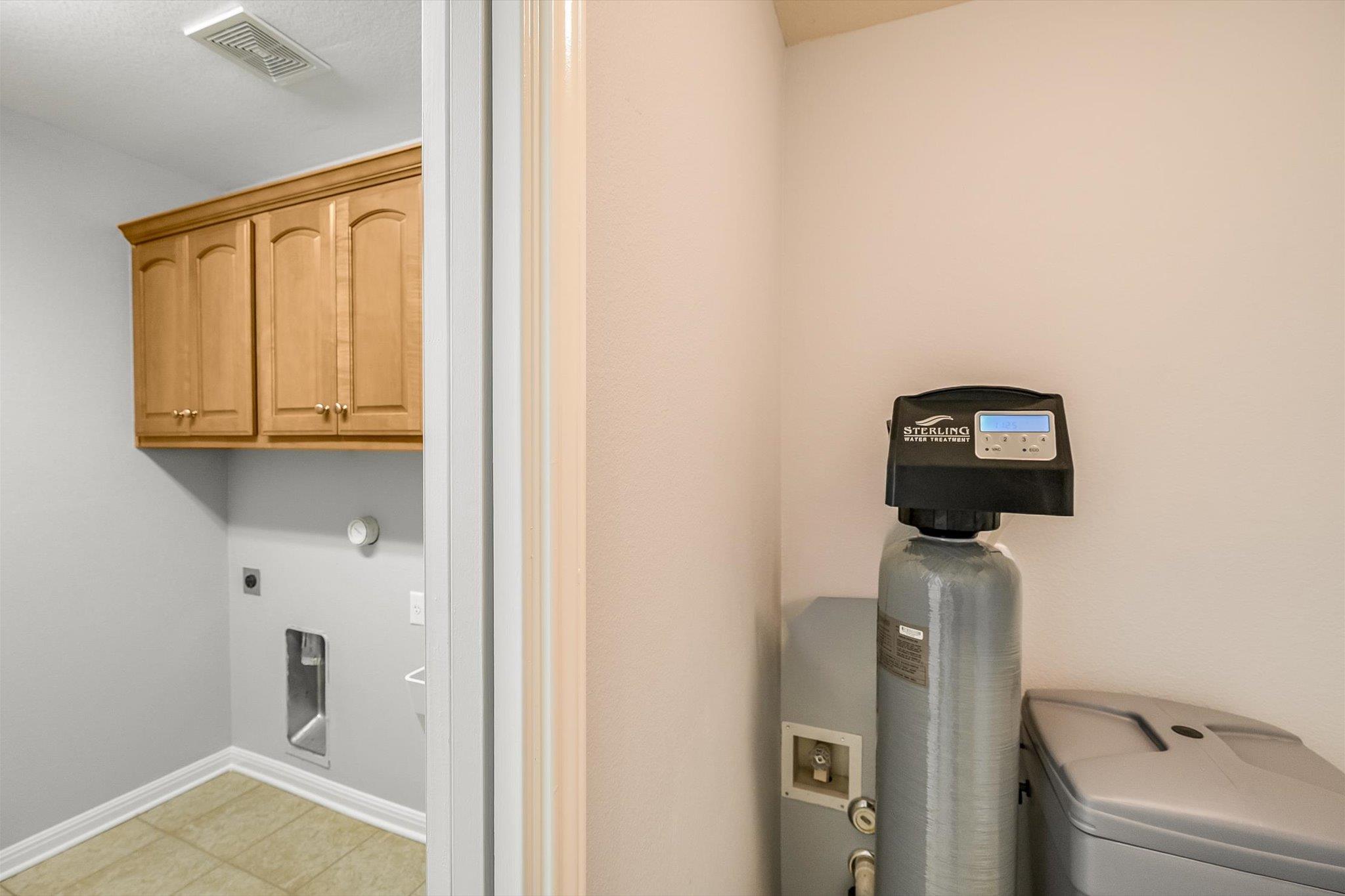 Laundry utility area with wooden cabinets, water softener, and washer.