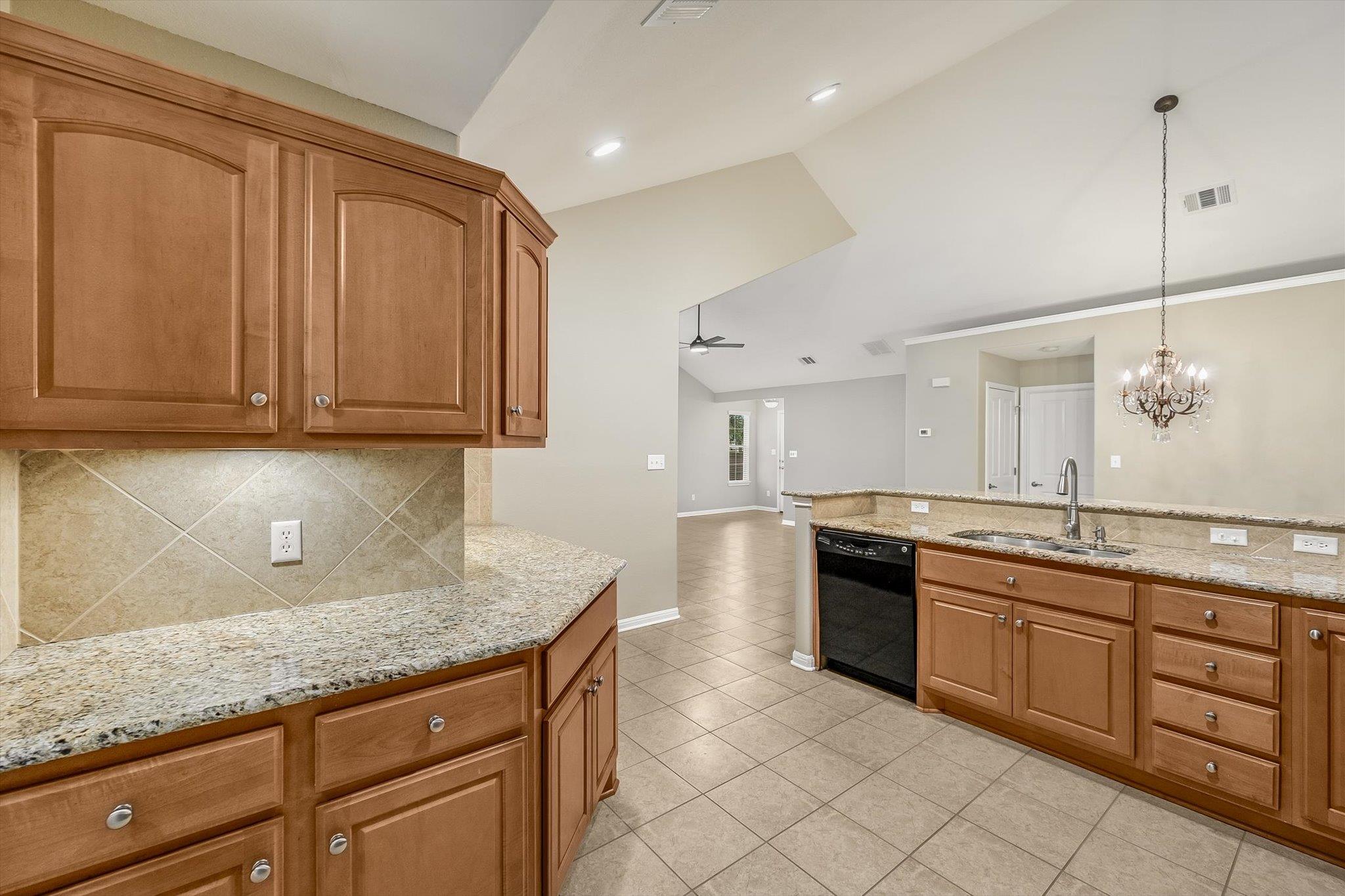 Kitchen with warm wood cabinets, granite countertops, tiled floors, and a sink peninsula opening to the living area.
